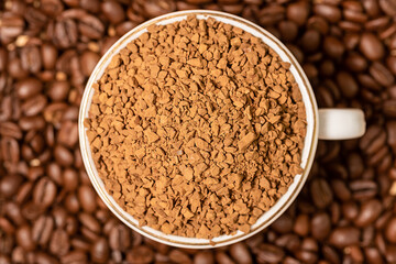 There is a white cup of ground coffee on top of the sprinkled beans. Close-up.