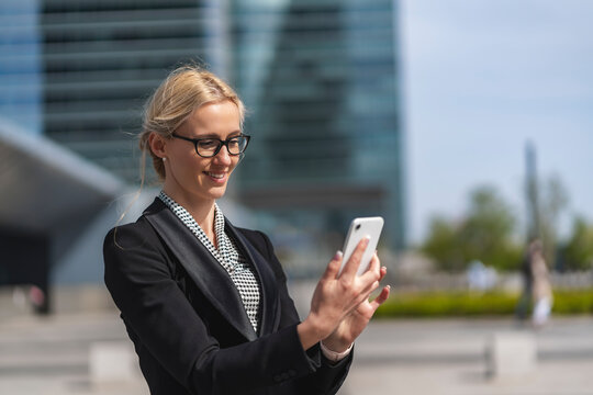 Mujer rubia ejecutiva con gafas feliz mirando el teléfono movil en el centro de negocios