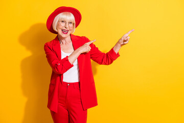 Photo portrait of senior woman wearing red suit headwear pointing fingers empty space isolated...