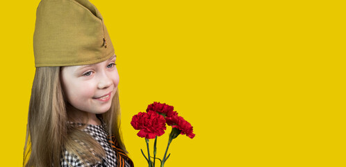 9th May. A little girl in a garrison cap with a St.George ribbon with red carnations stands on a...