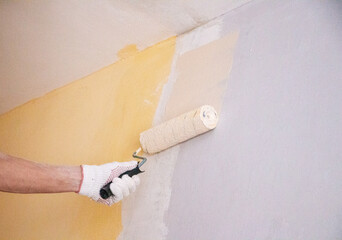 mans hand in cloth glove with paint roller applies fresh paint and primer to wall surface. process...