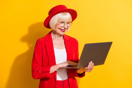 Photo portrait of senior business woman working on laptop in glasses red formal wear isolated vivid yellow color background