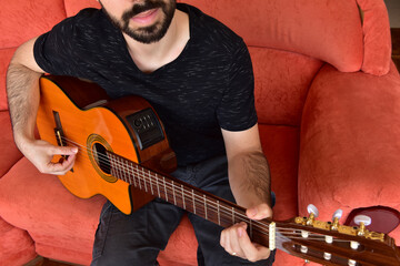 Obraz premium Boy playing music on acoustic guitar sitting on red sofa.