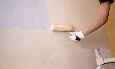 mans hand in cloth glove with paint roller applies fresh paint and primer to wall surface. process...