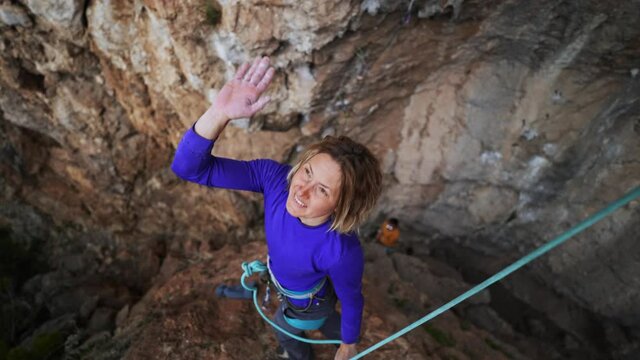 slow motion of joyful woman rock climber give high five after successful ascent of route on cliff. smiling woman wearing warm hat and showing thumb up to camera. 4k footage