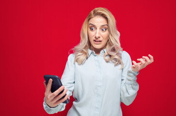 Rage girl using the mobile phone, isolated on red background. Furious young woman looks to...
