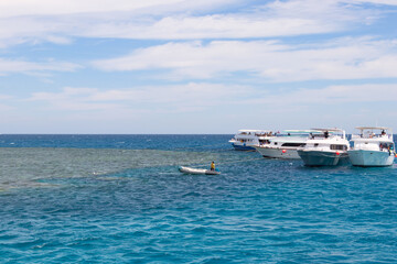 Fototapeta na wymiar Panoramic view of the Red Sea, coral reef and moored pleasure boats. Blue and white seascape, white boats and clear blue water with cloudy blue skies