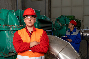 Young Worker in Red Coveralls and Hardhat Standing in Industrial Interior With Pipes and Generators