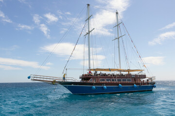 A pleasure sailboat plows the azure waters of the Red Sea, an imitation of a pirate ship, the sails are lowered, the blue sky with white clouds