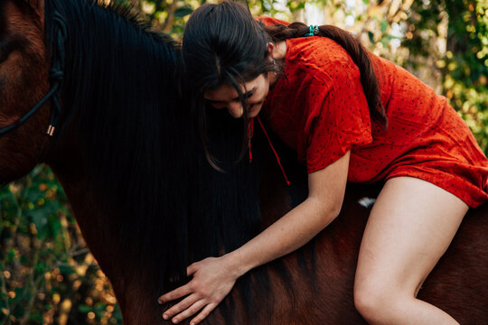 Beautiful young woman hugging brown horse and wearing dress