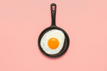 Fried egg in a frying pan on a pastel pink background. Top view, flat lay, copy space.