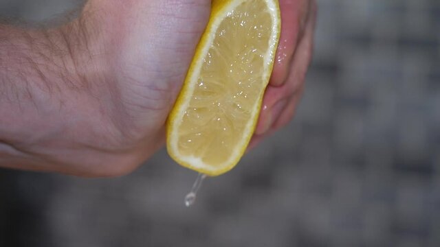 Male hand squeezing fresh lemon slow motion - juices pouring down