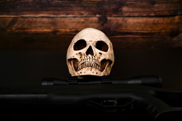The skull lies on the background of a sniper rifle with a scope. War and death concept.