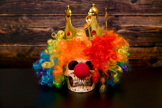 A skull with a red clown nose and a colored wig and a gold crown on its head.
