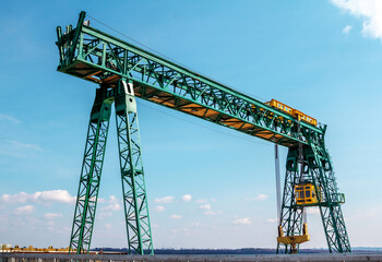 Fototapeta na wymiar Green gantry bridge crane at work over blue sky