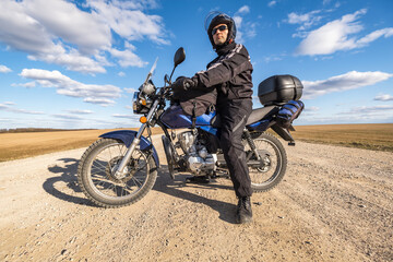  man in a black uniform on bike against the backdrop of panorama of field and blue sky. motorcycle travel concept