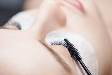Eyelash extension procedure with comb. Black fake long lashes beautiful woman eyes.