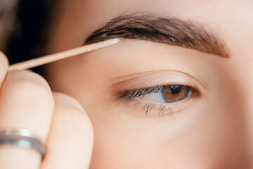 Correction and tint henna of eyebrows, master applies brush to woman marking on brow