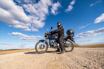 Naklejka na ściany i meble man in a black uniform on bike against the backdrop of panorama of field and blue sky. motorcycle travel concept