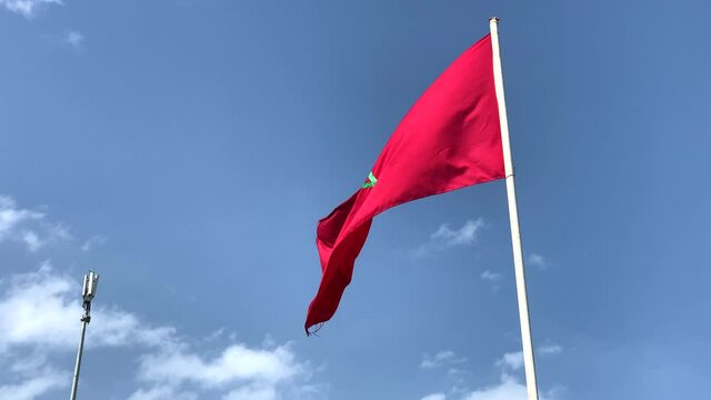 Real-time 4K footage of the Moroccan red flag waving around outdoors with a blue sky in the background