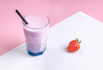 strawberry milk bubble tea in a glass with a straw and strawberry berry on a pink background