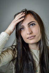 Portrait of a beautiful young woman with long brown hair who touches her head because she has forgotten something