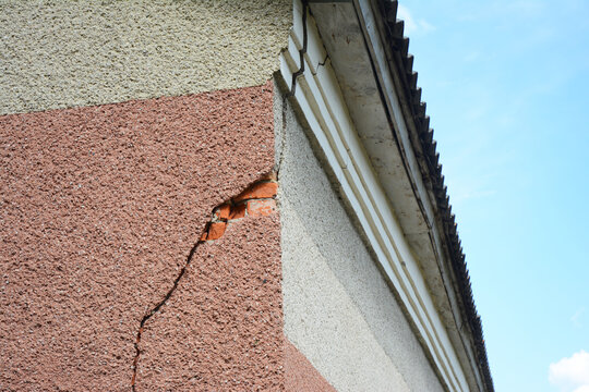 A serious stucco crack on the corner of the house near the rooftop. Repairing a stucco crack on the house wall.