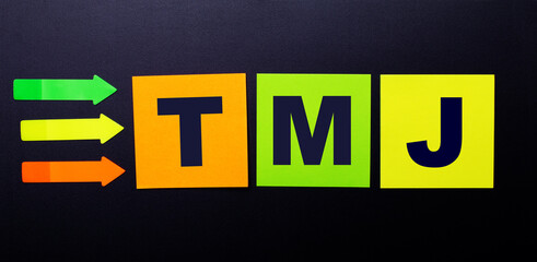 Bright multi-colored paper stickers on a black background with the text TMJ
