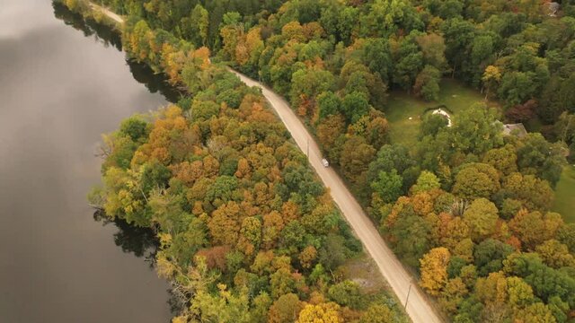 Aerial view of vintage fast food or ice cream truck moving on a lakeside road in countryside of early autumn