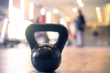Obraz na płótnie Canvas Panning shot showing a kettleball in focus with out of focus people in a gym with bright lights excercising as part of a healthy lifestyle and immunity and recovery from the coronavirus pandemic