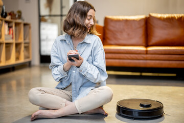 Relaxed woman with phone and robotic vacuum cleaner