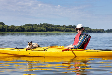 Domestic mekong bobtail (siames) cat enjoys freedom outside the house on kayaking in the river with owner in the summer morning in nature. A playful cat in an yellow kayak rests