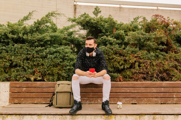 Happy young man with face mask using smartphone in the city. Medical mask.