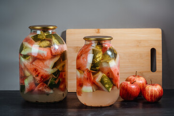 Pickled watermelon with apples in a glass jar on a wooden table