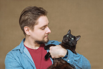 a young happy man with a beard holds a black cat in his hands close-up.the concept of pet love