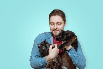 a young happy man with a beard holds two black cats on a blue background. the concept of pet love