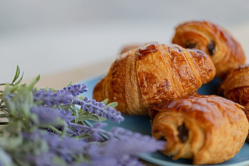 Tasty buns with raisins and french croissant. Dessert. Lavender flowers. Soft focus. Blurry background. Close-up. Macro.