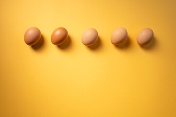 Row of raw eggs aligned on yellow background. Easter concept. Copy space