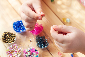 The child makes jewelry with his own hands, stringing colorful beads on a thread