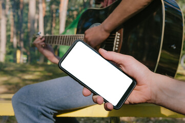 Mock up of a smartphone in front of a man playing the guitar. Against the background of the forest.