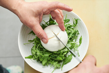 close up hand details of chef slicing burrata on a bed of arugula