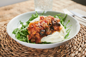 close up ready to eat burrata salad with tomato concasse and rucola on a rustic wooden table
