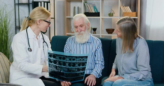 Adorable caring smiling skilled female doctor calming mature bearded man after she explaining the results of x-ray image and telling that his lungs is okey,man's wife is satisfied from news