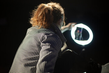 The girl removes the blog. The girl uses a round lamp to illuminate her face. Shooting a video blog...