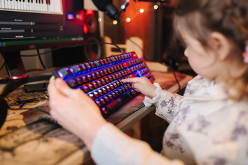 Closeup of little sister help brother and presses button on the keyboard with neon light. Little girl working on computer