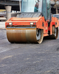 A heavy vibratory roller compresses hot asphalt in the working area of the roadway.