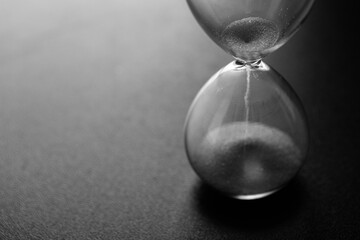 Sand passes through an hourglass measuring the travel time counting down to the deadline, black and white photo with space for text
