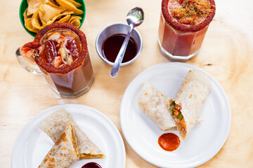 Mexican burrito and michelada beer with tomato juice with copy space. Michelada beer with tomato juice and burritos. Mexican food on wooden table. Concept of traditional food and mexican drink.