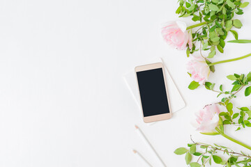 Flat lay home office desktop with notebook, pink tulips on a light background. Top view mockup smartphone with blank screen
