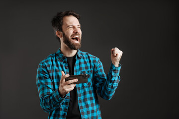 Fototapeta premium Excited man making winner gesture while playing online game on cellphone